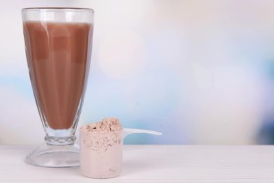 Whey protein powder and chocolate protein shake on table on bright background